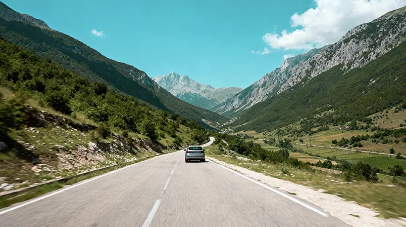 Scenic mountain road in Albania with rental car driving through valley with green hillsides