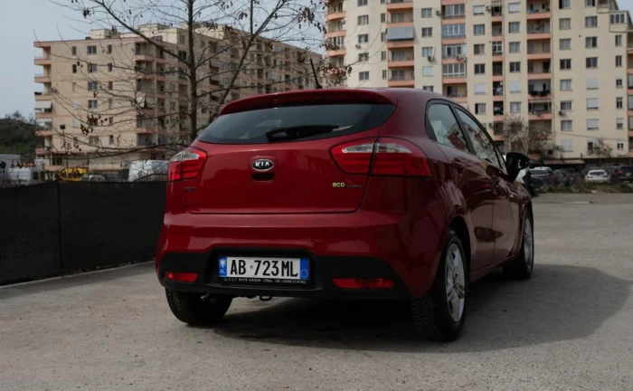 Rear three-quarter view of red Kia Rio 2014 1.2 petrol manual rental car showing hatchback and Albanian license plate