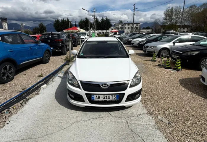 White Hyundai i30 2010 1.6 diesel manual hatchback rental car parked near Tirana International Airport Rinas with air‑conditioned interior