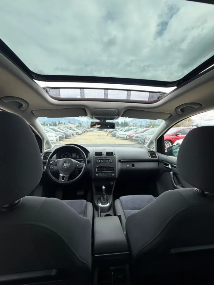 Interior of VW Touran 2013 7-seater rental showing panoramic sunroof, dashboard, steering wheel and automatic transmission
