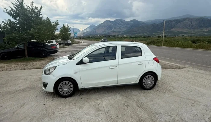 White Mitsubishi Space Star 2017 1.0 petrol manual 5‑door hatchback parked near Albanian mountains and Tirana Airport, available for car rental with TiRental