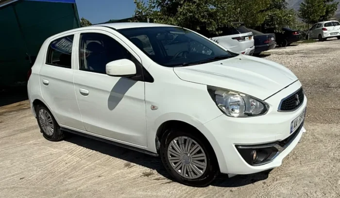 White Mitsubishi Space Star 2017 1.0 petrol manual 5‑door hatchback parked near Albanian mountains and Tirana Airport, available for car rental with TiRental