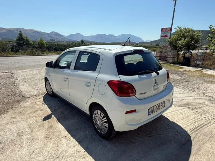 White Mitsubishi Space Star 2017 1.0 petrol manual 5‑door hatchback parked near Albanian mountains and Tirana Airport, available for car rental with TiRental