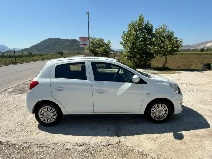 White Mitsubishi Space Star 2017 1.0 petrol manual 5‑door hatchback parked near Albanian mountains and Tirana Airport, available for car rental with TiRental