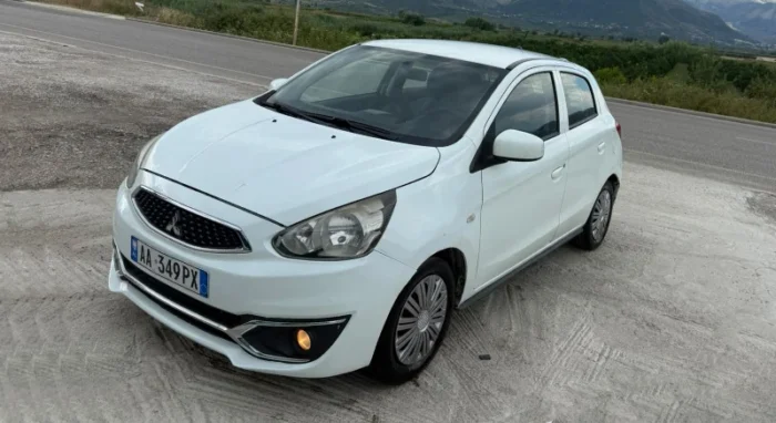 White Mitsubishi Space Star 2017 1.0 petrol manual 5‑door hatchback parked near Albanian mountains and Tirana Airport, available for car rental with TiRental
