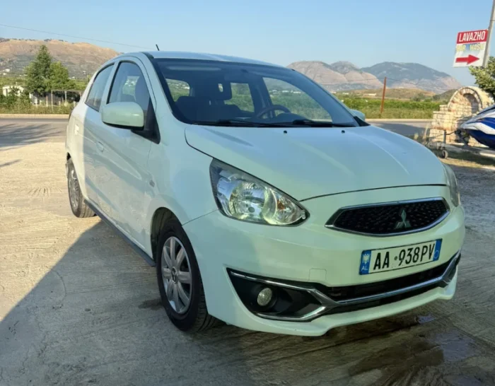 White Mitsubishi Space Star 2017 1.0 petrol manual five‑door hatchback parked near Albanian mountains and Tirana Airport, available for car rental with TiRental