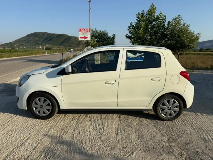 White Mitsubishi Space Star 2017 1.0 petrol manual five‑door hatchback parked near Albanian mountains and Tirana Airport, available for car rental with TiRental