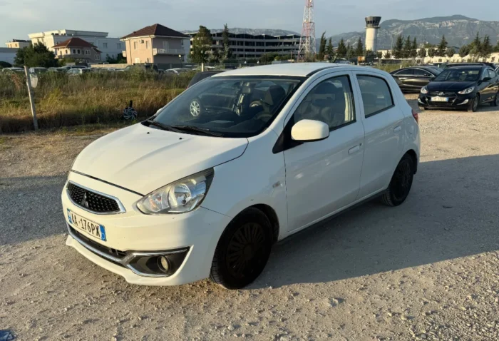 White Mitsubishi Space Star 2017 1.0 petrol manual 5‑door hatchback parked near mountains and Tirana Airport, available for car rental in Albania with TiRental