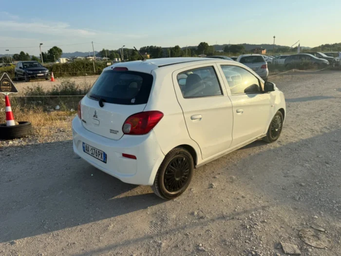 White Mitsubishi Space Star 2017 1.0 petrol manual 5‑door hatchback parked near mountains and Tirana Airport, available for car rental in Albania with TiRental